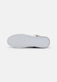 White sneaker sole with textured grip pattern, featuring a brown side accent. Curved shape, smooth rubber material, and minimal design.