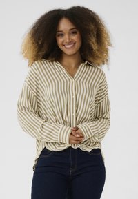 Camisa de botones a rayas en beige y blanco, con un corte relajado, mangas largas y puños. Combinada con jeans oscuros.