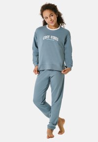 Hellblaues Sweatshirt und Jogger-Set. Das Sweatshirt hat den weißen Schriftzug "COSY VIBES". Die Jogger verfügen über elastische Bündchen. Weicher, glatter Stoff.