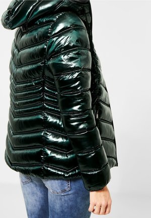 Doudoune vert foncé brillante avec couture horizontale matelassée, portée avec un jean bleu, vue de dos et de côté.