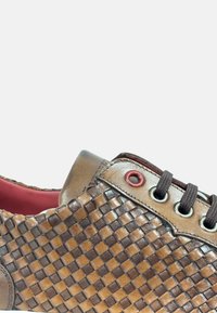 Zapatilla de cuero trenzado marrón con acentos rojos, punta redonda y cordones oscuros. Presenta una superficie texturizada y un color interior contrastante.