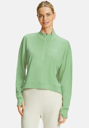 Groene pullover van soepel materiaal, met een hoge kraag, halve rits en een ontspannen pasvorm. Logo "FALKE" is in het wit op de voorkant gedrukt.