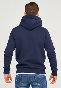 Mörkblå huvtröja med en stor huva och långa ärmar. Tillverkad av mjukt material med ribbade mudd och nederkant, med sömmar som detalj.