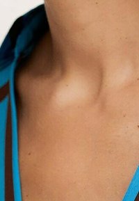Acercamiento al escote con un tono de piel suave, destacado por una camisa de tela azul con acentos marrones oscuros y un corte relajado.