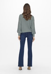 Grå stickad tröja med puffärmar, kombinerad med mörkblå utsvängda jeans. Slät textur, figurnära passform och subtila ribbade detaljer i nederkant.