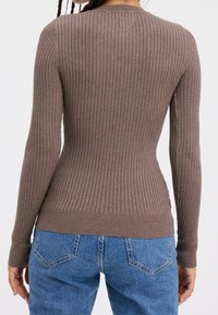 Maglietta a maniche lunghe rib corda marrone con vestibilità attillata e scollatura rotonda, caratterizzata da un motivo a maglia testurizzata, abbinata a jeans blu a vita alta.