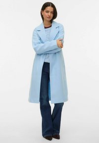 Hele sinine trentšmantel, millel on pikk ja avar lõige, laiad kraeäärised ning küljel taskud, kantud sinise kampsuni ja tumedate lahkuvate teksapükste kohal.