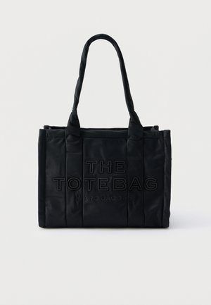 Črna pravokotna torba z oblazinjenimi ročaji in vtisnjenim napisom "THE TOTE BAG MARC JACOBS" na prednji strani.