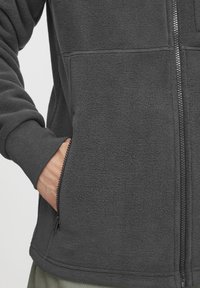 Dark grey fleece jacket with a full-length zipper, ribbed cuffs, and side pockets. Fabric has a soft, textured surface.