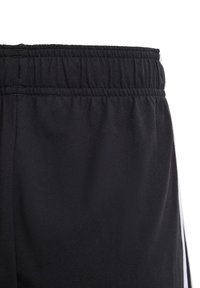 Pantalones cortos deportivos negros con cinturilla elástica y rayas blancas a los lados. La tela es suave y con un ligero brillo.