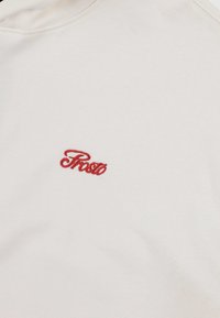 Biała bawełniana koszulka z okrągłym dekoltem i czerwonym haftowanym logo "Prosto" na środku. Miękka tekstura z gładkim wykończeniem.