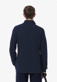 Mørkeblå langermet skjorte med krage, med rett snitt og knappede mansjetter. Glatt tekstur, minimal detaljer bak.
