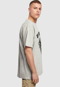 Šedé bavlněné tričko s krátkými rukávy, s potištěným černým grafickým designem na přední straně. Volný střih, kulatý výstřih.