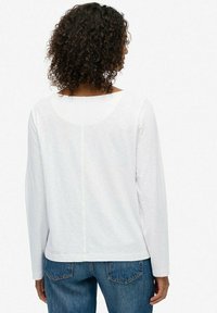 Witte long-sleeve top van lichte stof, met een boot halslijn en een verticale naad op de rug, gecombineerd met blauwe jeans.