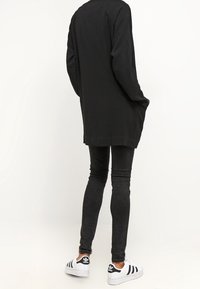 Svart långärmad topp med lös passform, kombinerad med tighta svarta jeans och vita sneakers med svarta ränder och logotypdetaljer.