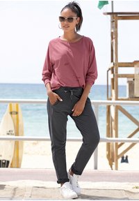 Lässiges Outfit mit einem rosefarbenen Langarmoberteil und dunkelgrauen Jogginghosen mit Kordelzug. Weiße Sneaker runden den Look ab.