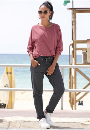 Lässiges Outfit mit einem rosefarbenen Langarmoberteil und dunkelgrauen Jogginghosen mit Kordelzug. Weiße Sneaker runden den Look ab.