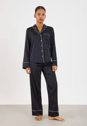 Mustast satiinist pajama komplekt, millel on pikad varrukad, tasku ja valged äärised kraes ja mansettides. Lõdvad püksid otse säärekujuga.