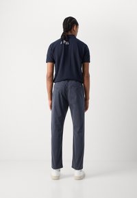 Mörkblå polo med korta ärmar, med en liten design vid halsen; kombinerad med grå byxor och vita sneakers med synlig logotyp.