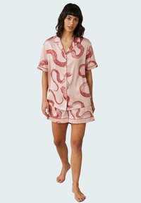 Light pink silk pajama set featuring red snake patterns. Short-sleeve shirt with collar and button closure, paired with matching shorts.