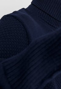 Maglione lavorato a maglia blu navy con corpo testurizzato, colletto alto a coste e maniche lisce, che mette in risalto dettagli in tessuto a contrasto.