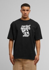 Sort bomulds t-shirt med korte ærmer, der har et hvidt grafisk design, som inkluderer ordene "market studios" og en globusillustration.