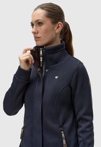 Mornarska zip-up jakna iz teksturirane tkanine, z visokim ovratnikom, srebrnimi dodatki in stranskimi žepi. Akcentni logotip na prsih.