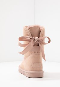 Bota de ante rosa con un suave forro de piel, que presenta un gran lazo de satén en la parte trasera y una suela de goma texturizada. Diseño minimalista.
