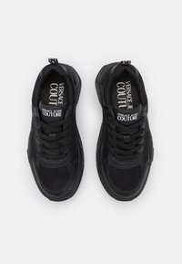 Svarta sportiga sneakers med ett mesh-ovandel, snörningsdesign, vadderad krage och präglad brandlogga på tungan och innersulan.