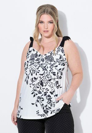 Top con patrón floral en blanco y negro con lazos en los hombros, que presenta un diseño de escote en V y bolsillos frontales, combinado con pantalones negros de lunares.