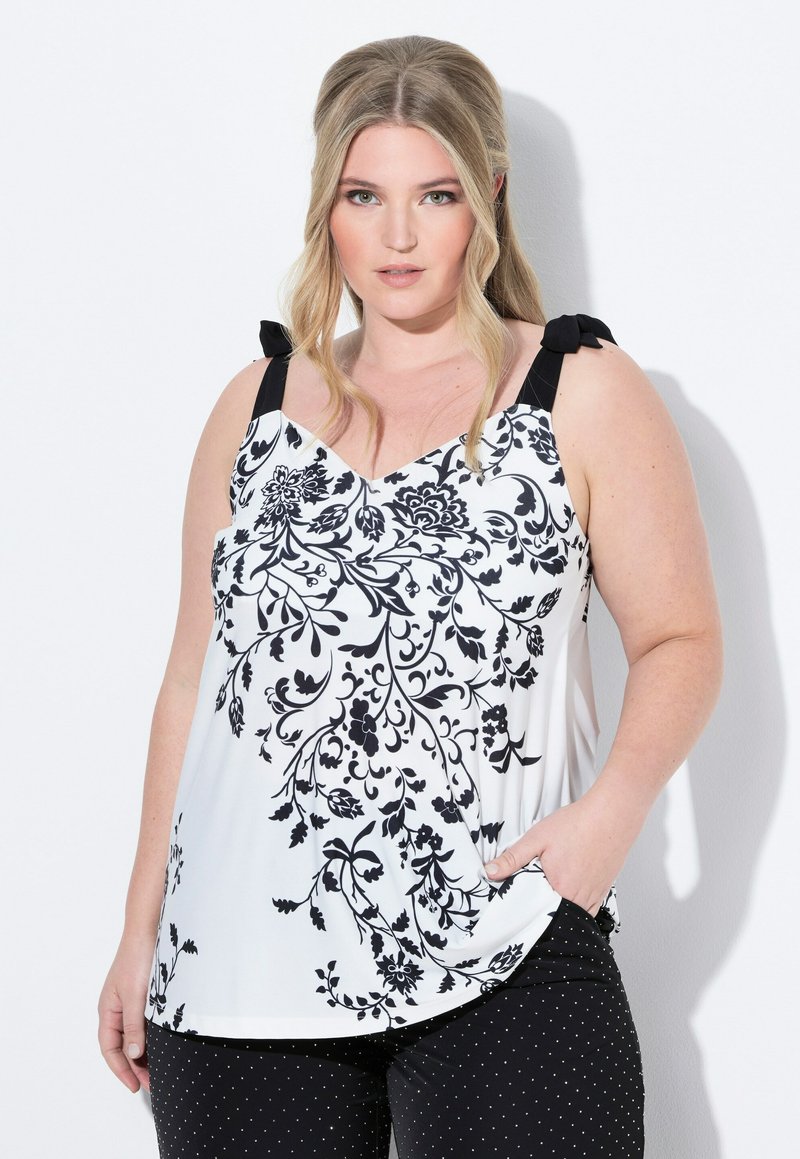 Top a fiori in bianco e nero con fiocchi sulle spalle, caratterizzato da un design a V e tasche frontali, abbinato a pantaloni a pois neri.