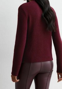 Maglione a coste bordeaux con maniche lunghe e vestibilità rilassata, caratterizzato da un colletto rotondo e un motivo di tessuto testurizzato.
