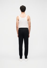 Μαύρο παντελόνι φόρμας με ελαστική μέση και πίσω τσέπη, σε συνδυασμό με λευκό αμάνικο τοπ. Το μοντέλο φαίνεται από πίσω.