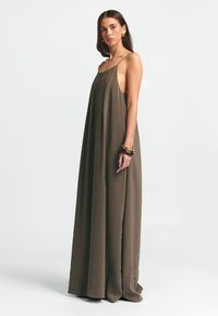 Lång, ärmlös klänning i olivgrön tyg, med en lös passform och sidokut för luftgenomströmning. Enkel design utan synliga mönster.