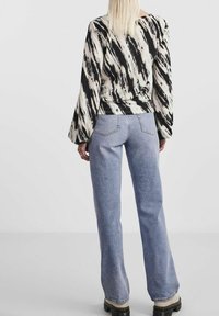 Långärmad topp med svartvit abstrakt mönster, i kombination med ljusblå högmidjade vida jeans. Svarta kraftiga stövlar syns.