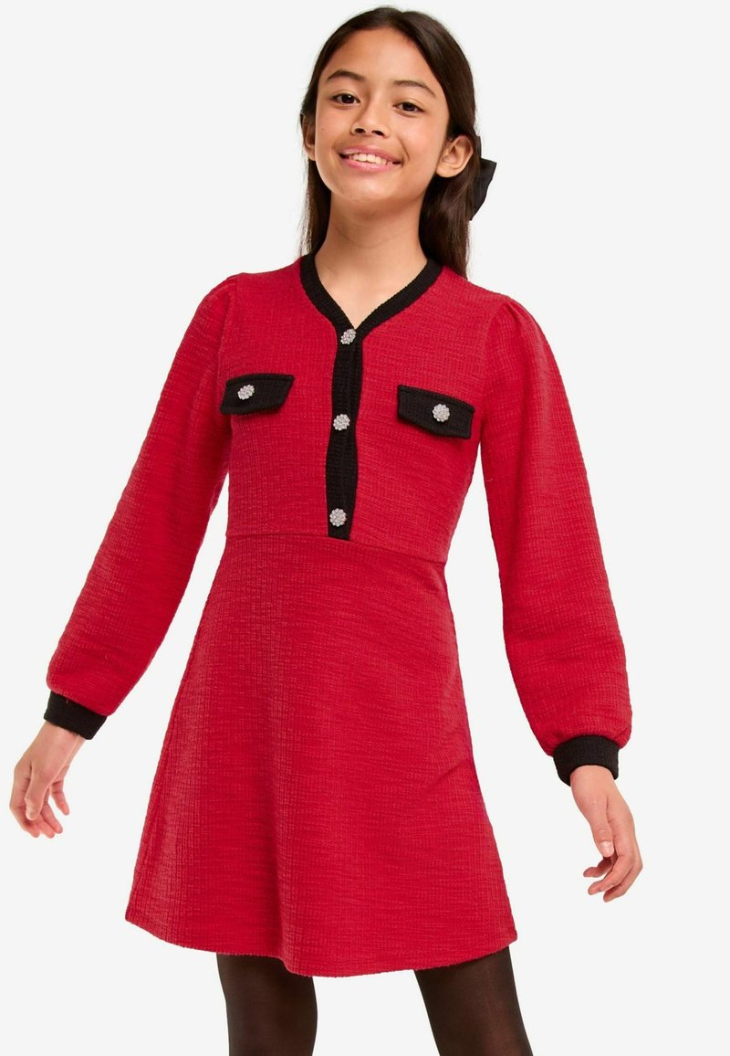Rotes Kleid mit strukturierter Oberfläche, schwarzem Akzent und zwei Brusttaschen. Hat lange Ärmel und ist knielang mit Knopfdetails.