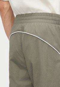 Κοντινό πλάνο ενός ατόμου που φοράει παντελόνι ελιάς με ελαστική μέση και λευκή περίγραμμα στο πίσω μέρος.