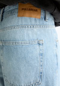 Jeans de mezclilla azul claro con una etiqueta de parche que dice "PULL&BEAR," con un bolsillo trasero y detalles de costura visibles.