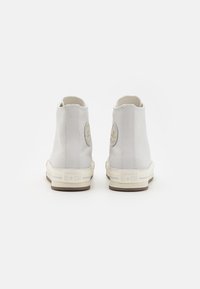 Hvite lerrets høye sneakers med beige gummisåler, med en sirkulær logo-patch og minimal stikning.