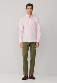 Camisa de botones rosa claro, diseño ajustado, mangas largas, combinada con pantalones slim fit de color verde oliva y zapatos marrón oscuro. Tejido simple con textura.