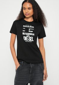 Čierne tričko s krátkym rukávom s výrazným bielym nápisom a unikátnym výrezom na hrudi. Mäkká látka s voľným strihom.