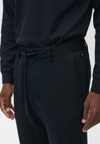 Pantalons bleu marine foncé en tissu texturé, dotés d'une taille à cordon de serrage, de poches latérales et d'une coupe ajustée.