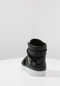 Czarne sneakersy za kostkę z ekoskóry z teksturą krokodyla, z wieloma srebrnymi klamrami i białą gumową podeszwą.