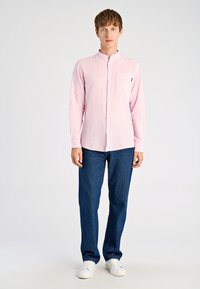 Lichtroze shirt met lange mouwen, een opstaande kraag en een borstzak, gecombineerd met donkerblauwe jeans en witte sneakers. Gladde textuur.