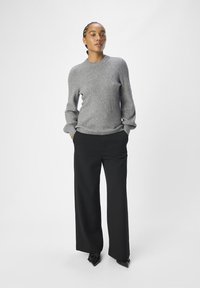 Gray knitted sweater featuring a ribbed texture and diagonal pattern, paired with black wide-leg trousers and pointed black shoes.