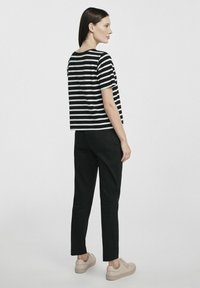 Czarna i biała w paski koszula z krótkim rękawem w połączeniu z czarnymi spodniami i beżowymi sneakersami. Koszula ma luźny krój i okrągły dekolt.