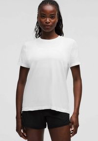 Weißes Kurzarm-T-Shirt mit rundem Ausschnitt und subtiler Rippstruktur, kombiniert mit schwarzen Shorts in einem lockeren Schnitt.