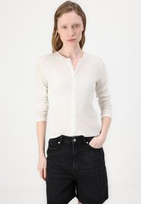 Hvit langermet strikket topp med rund hals og knappestolpe, paret med høy midje svarte denimshorts. Glatt tekstur, lett stoff.