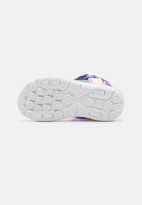 Zapatilla colorida con una suela de goma blanca texturizada, que presenta patrones hexagonales y una parte superior multicolor con correas azules, moradas y rosas.