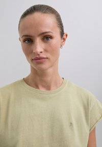 Light green cotton T-shirt with rolled sleeves and a crew neckline, featuring a small embroidered skull design on the chest.